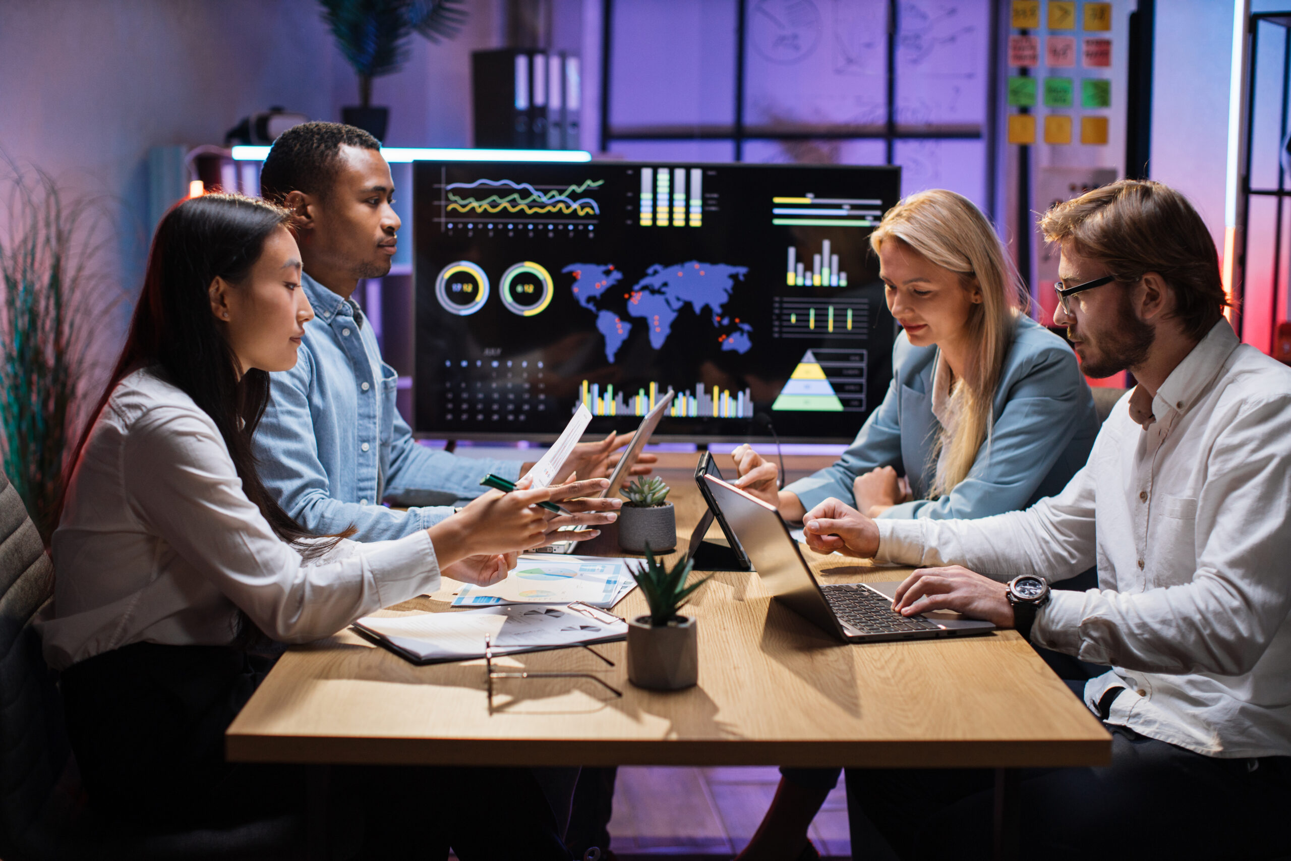International team of competent financiers using modern tablets and laptops while having meeting at modern office. People working with financial charts and graphs. Business and technology concept.