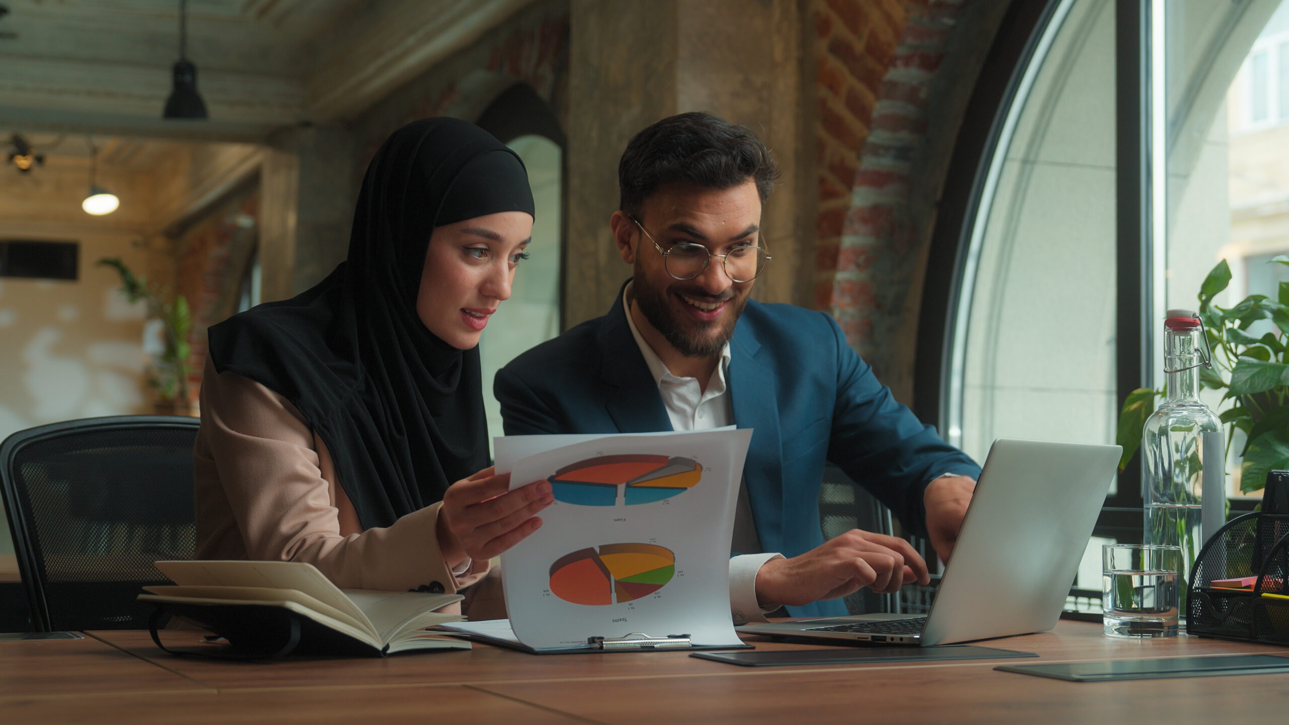 Male female teamwork Arabian man muslim woman in hijab girl guy businessman businesswoman two happy business colleagues coworkers managers analyzing marketing graphs documents in office typing laptop. High quality 4k footage